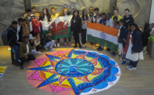 Grwp o blant o Gymru ac India yn sefyll gyda'u gwaith celf rangoli.